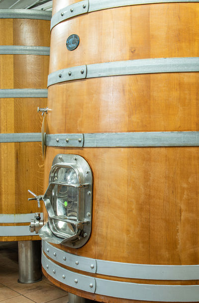 Detail velkého dřevěného sudu s kovovým armováním a kovovým ventilem určeného pro výrobu vína.